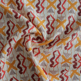 Close up of gently draped printed fabric with red squiggles, pink striped triangles, orange  X marks on a broken grid in orange on a white background. 