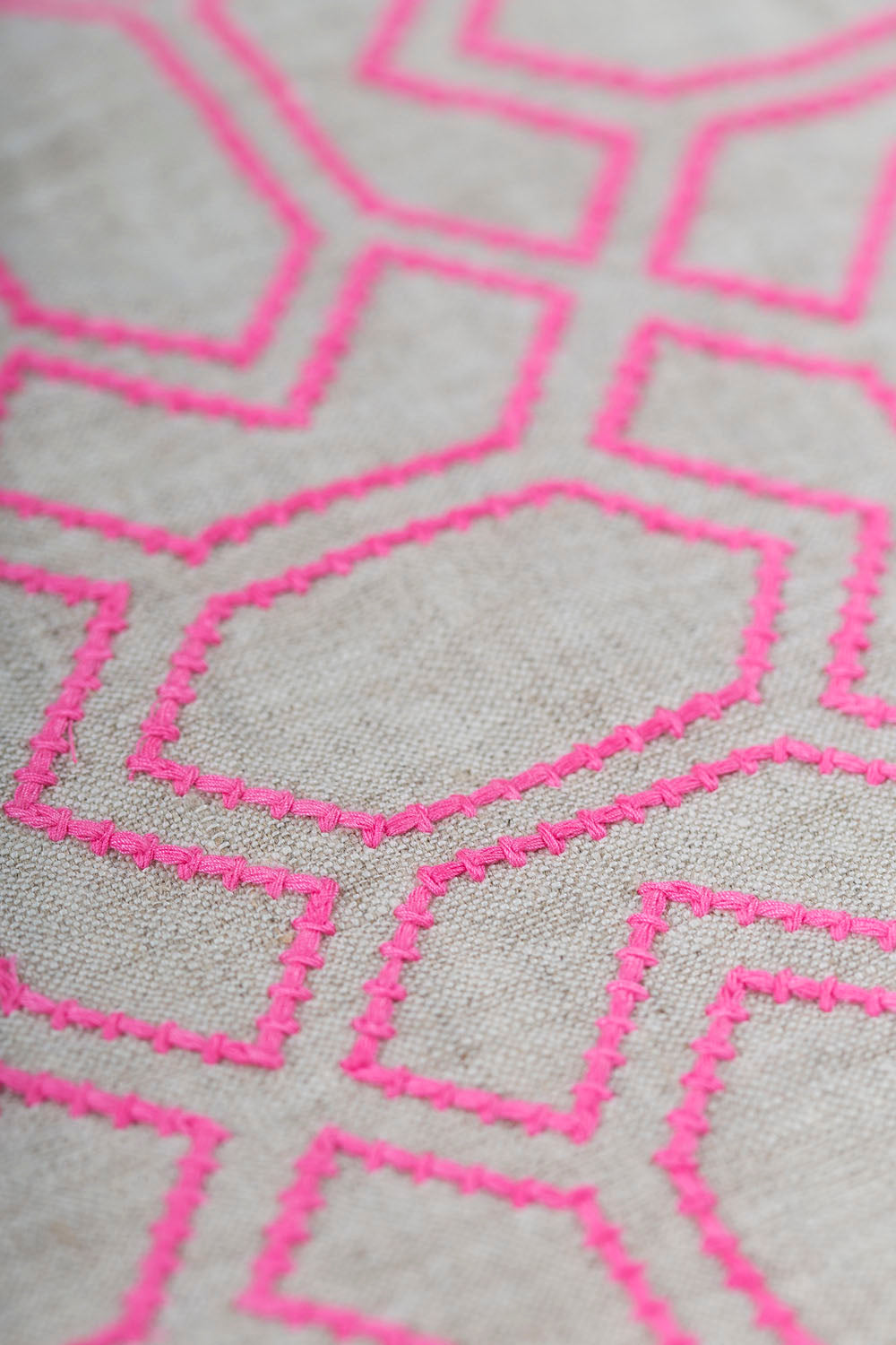 Detail of fabric with an embroidered geometric grid print in pink on a gray field.