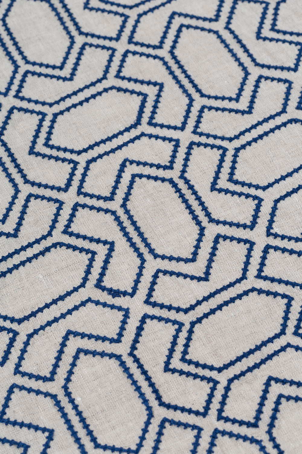Detail of fabric with an embroidered geometric grid print in navy on a light gray field.