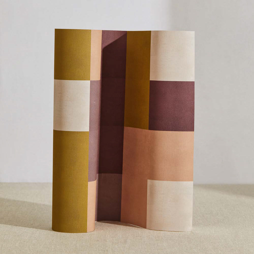 A curved partition stands on the ground, covered in an interlocking square pattern in shades of mustard, purple and pink.