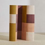 A curved partition stands on the ground, covered in an interlocking square pattern in shades of mustard, purple and pink.