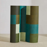 A curved partition stands on the ground, covered in an interlocking square pattern in shades of turquoise, green and cream.