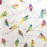 Detail of fabric in a painterly bird and branch print in green, yellow, pink and black on a white field.