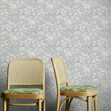 Two wooden chairs with wicker backs against a pale blue floral wallpapered wall.