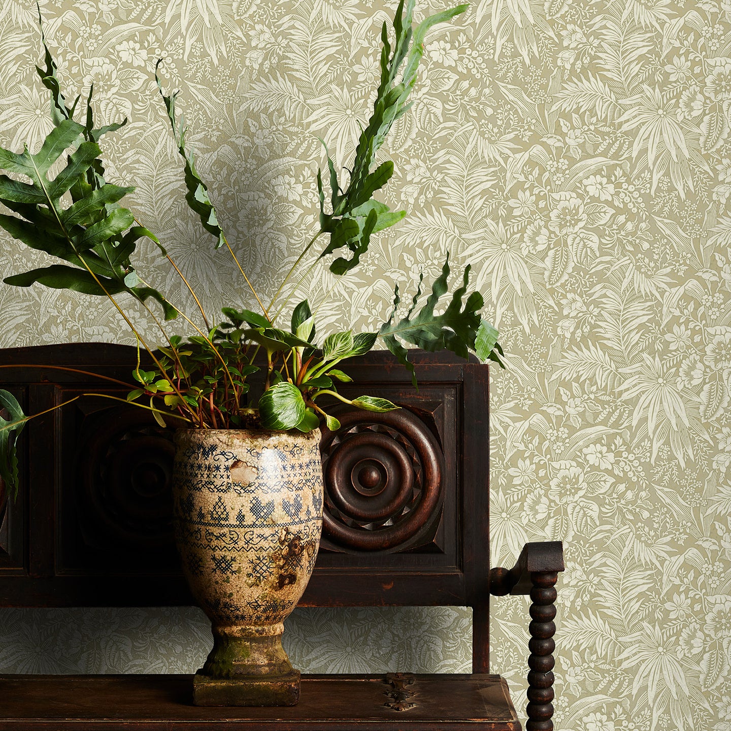 Potted plant on a wooden cabinet with decorative taupe floral wallpaper in the background