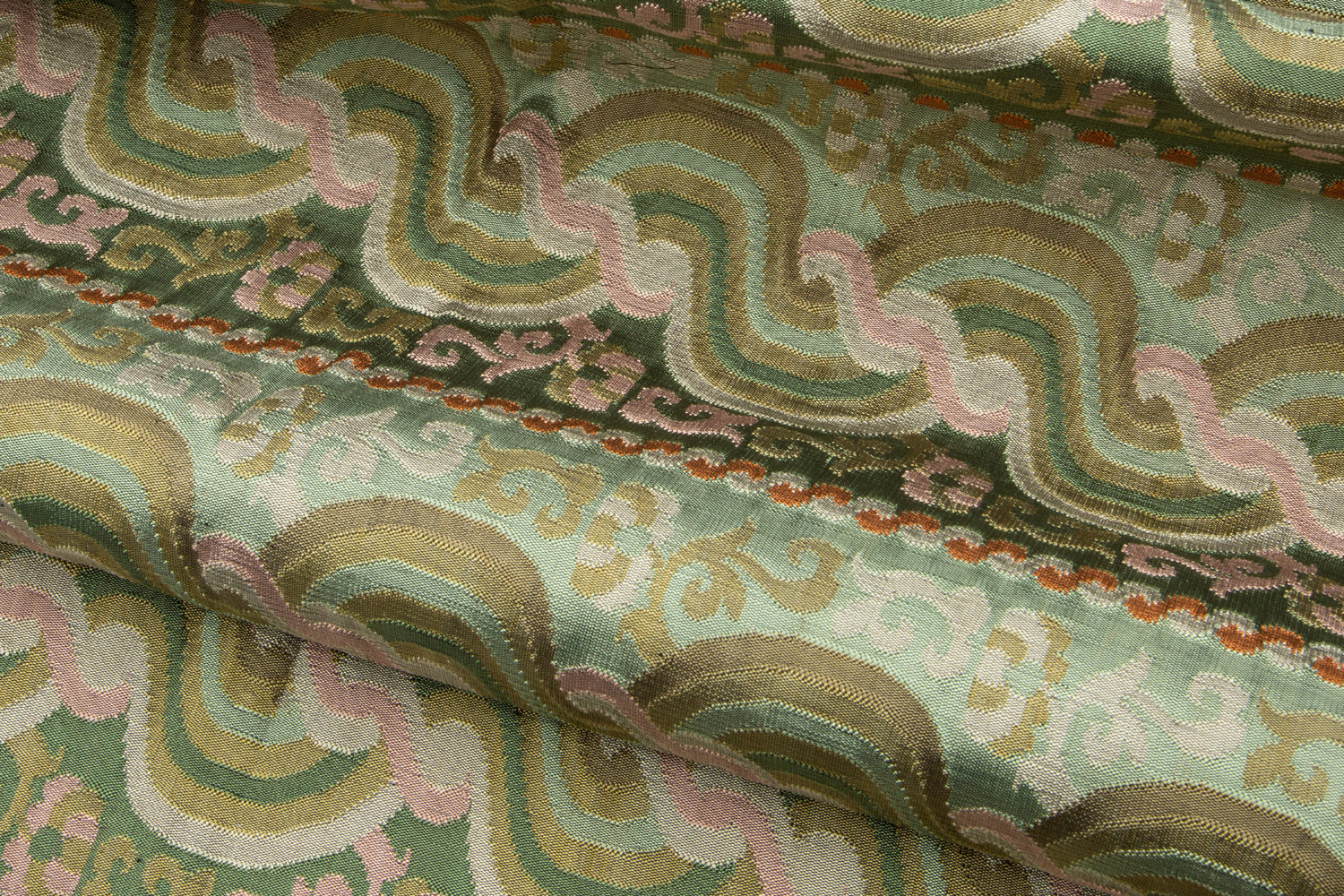 Close-up of folded handwoven silk fabric with wavy patterns in green, pink, and tan.