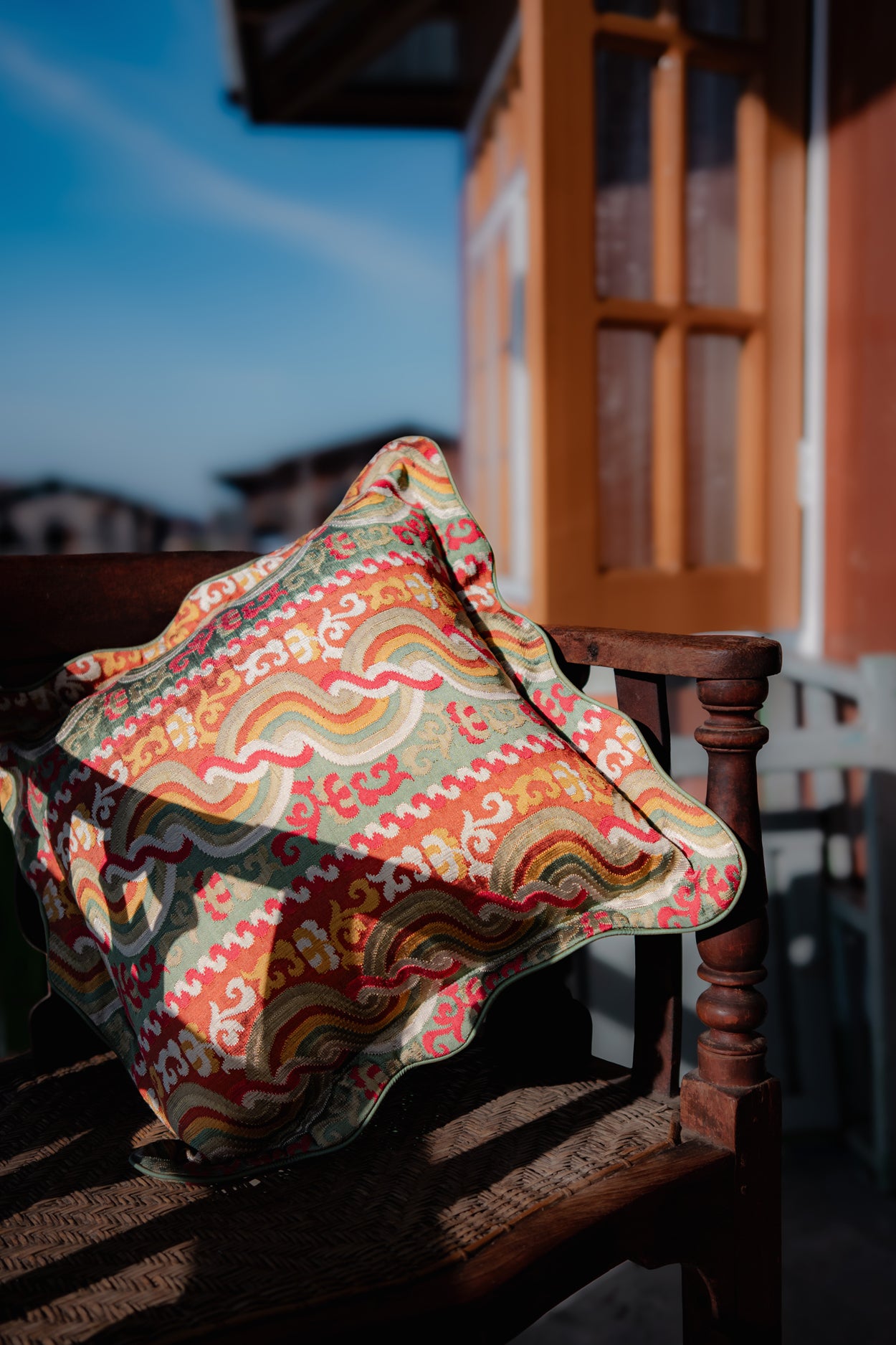 Colorful patterned fabric pillow on a wooden chair with a blurred outdoor setting
