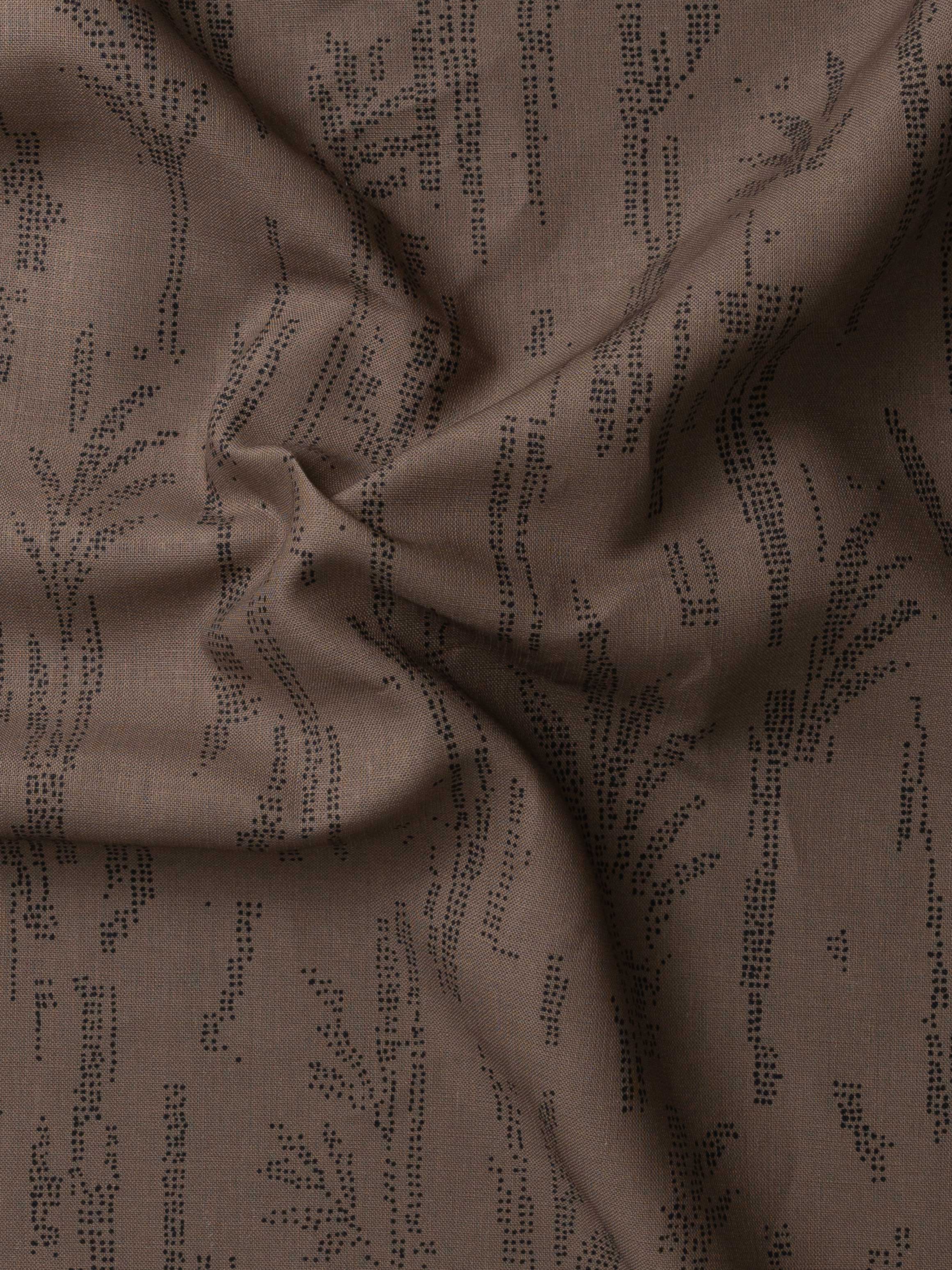 Detail of gently draped printed fabric with a black pointillist wheat frond pattern on a warm brown background. 