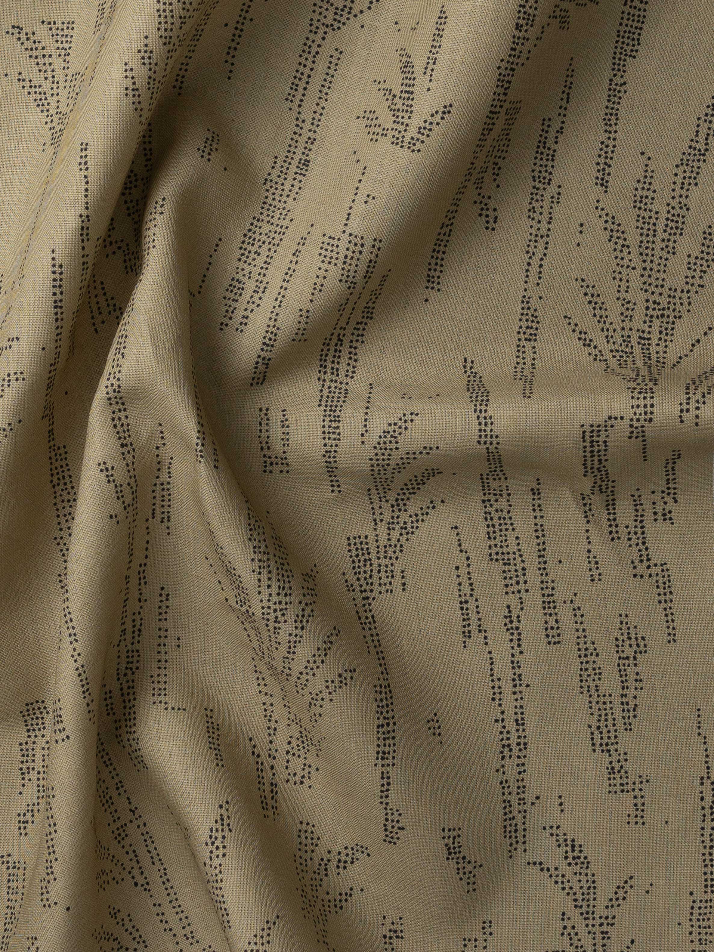 Detail of gently draped printed fabric with a black pointillist wheat frond pattern on a muted ochre background. 
