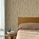 Bed with tan linens and wooden headboard, wooden side table  with white book and green glass, white floor length curtain against a black pointillist wheat frond patterned wallpaper on a tan background. 