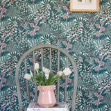 A wooden chair stands in front of a wall papered in a dense floral print in turquoise, pink and yellow.
