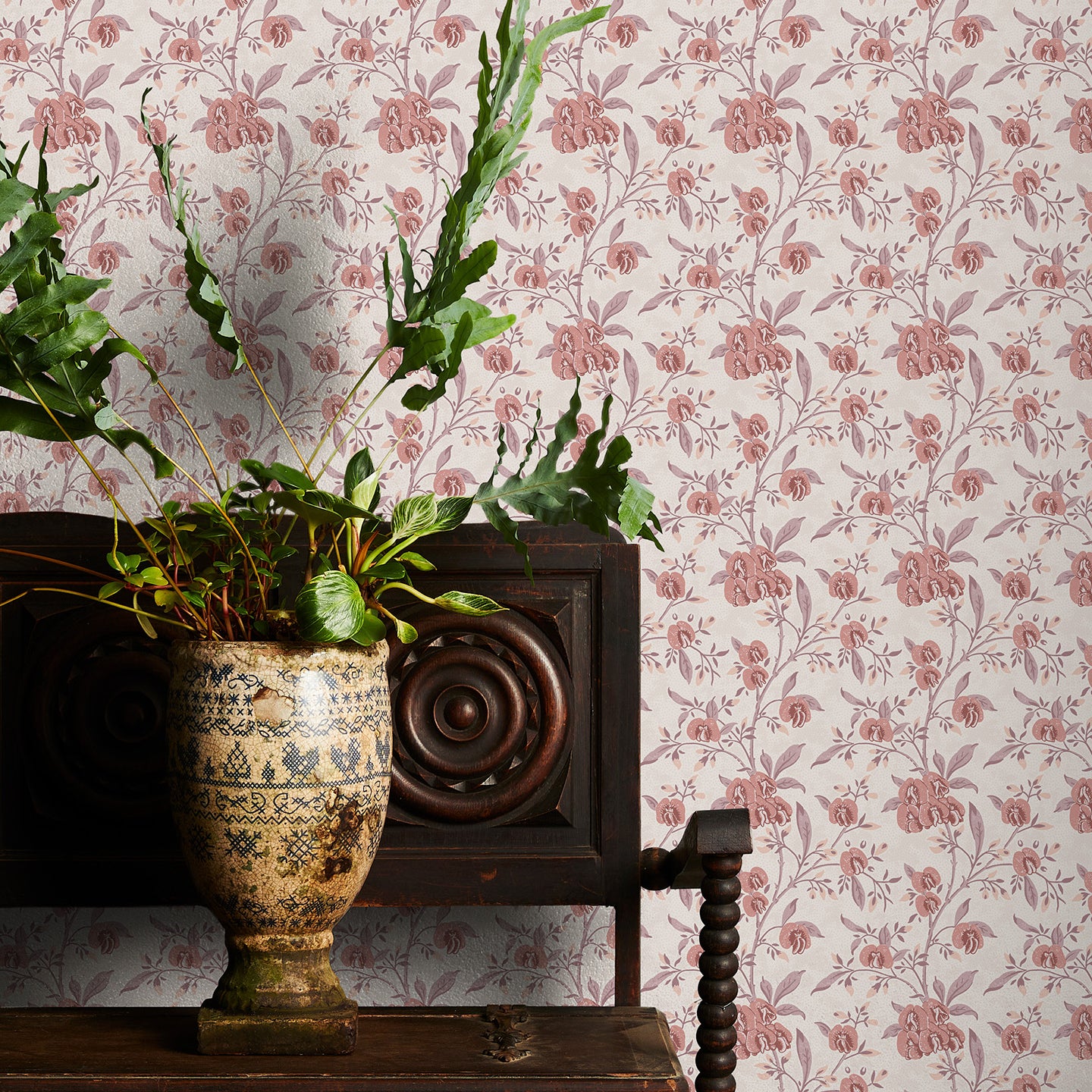 Decorative plant in a vase on a wooden table with pink floral wallpaper in the background