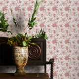 Decorative plant in a vase on a wooden table with pink floral wallpaper in the background