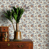 Decorative wallpaper with brown and blue floral pattern, wooden dresser with brass vase and plant, and small statue.