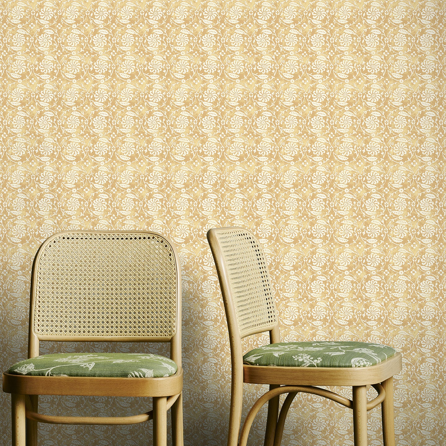 Two wooden chairs with green cushions against a yellow floral wallpapered wall.