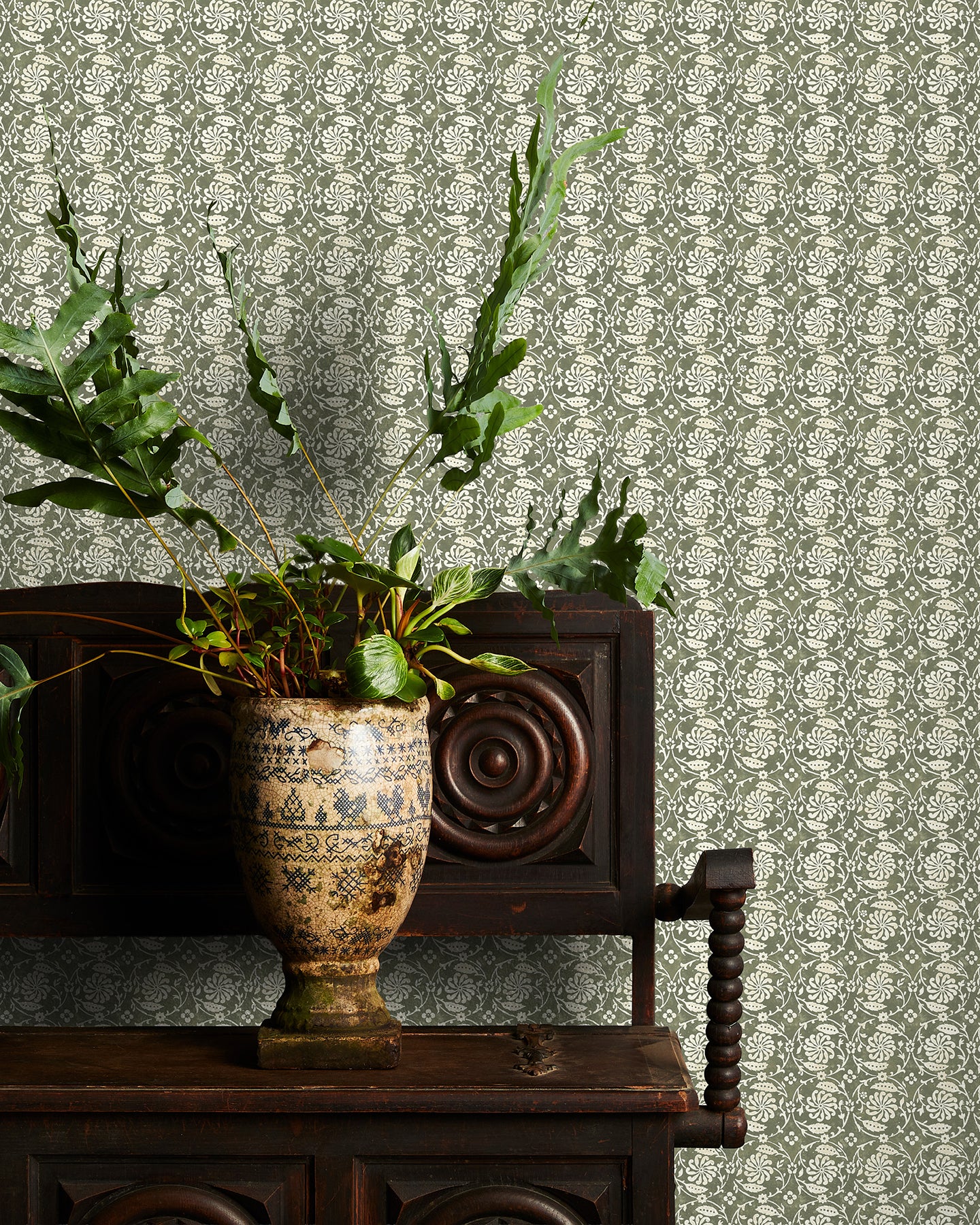 Decorative green floral wallpaper with a subtle pattern, potted plant on a wooden cabinet.