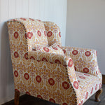 Upholstered chair in a floral pattern in orange and red on cream against white panelled wall. 