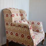 Upholstered chair in a floral pattern in orange and red on cream against white panelled wall. 