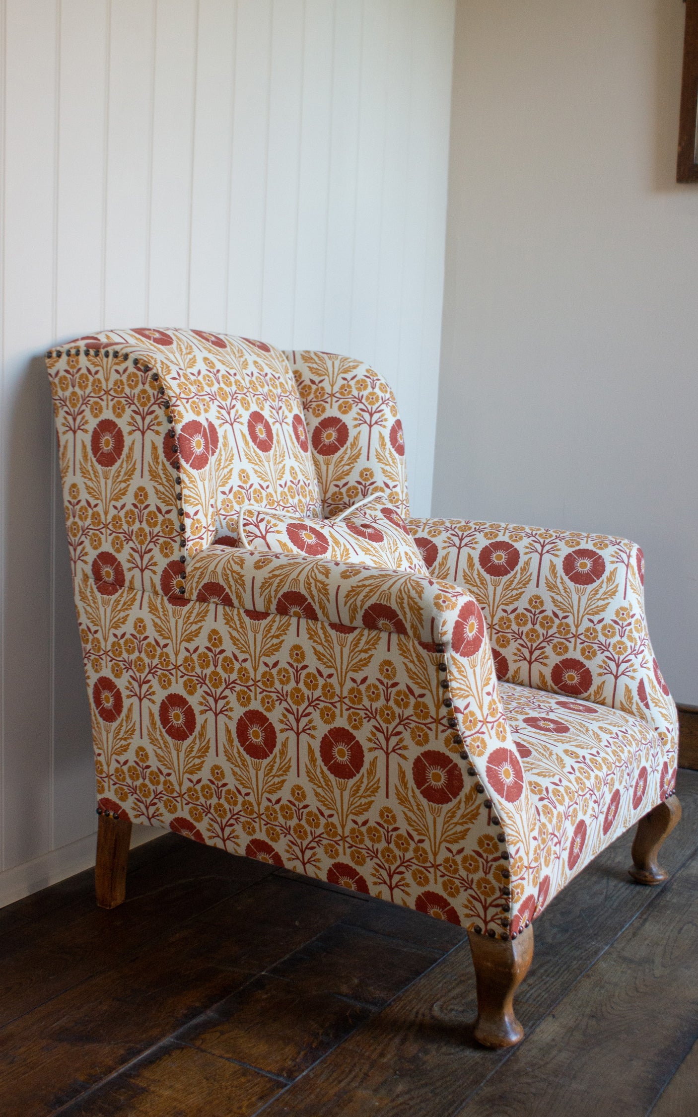 Upholstered chair in a floral pattern in orange and red on cream against white panelled wall. 
