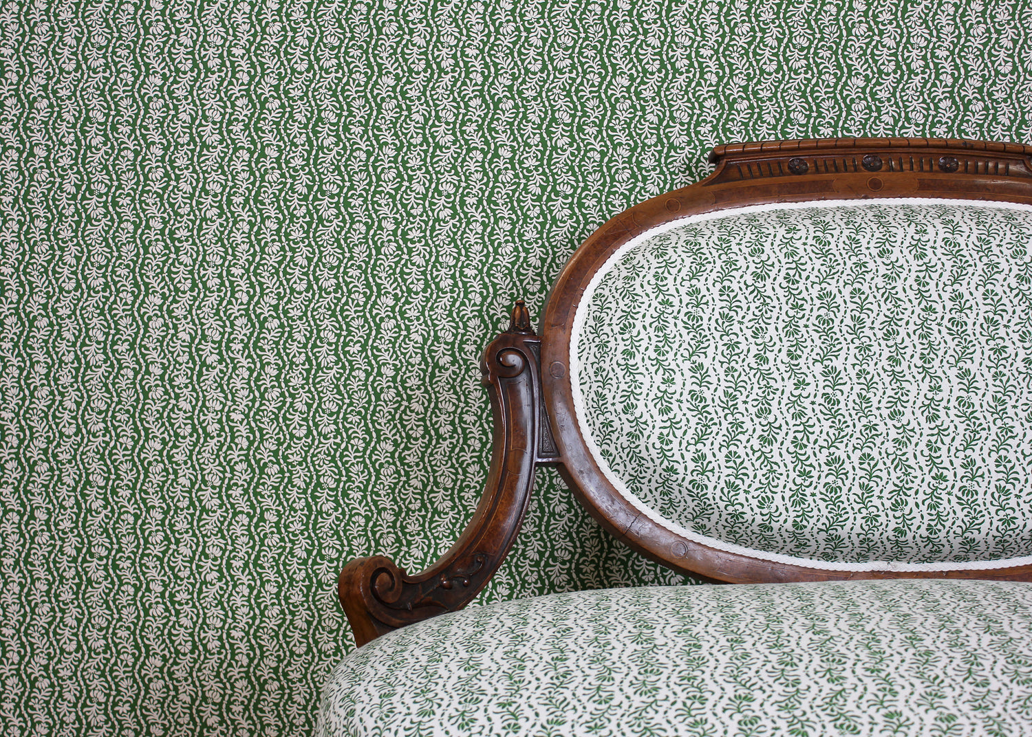 Ornate settee in a wavy floral stripe design in green on white against wallpaper in the same design. 