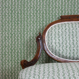 Ornate settee in a wavy floral stripe design in green on white against wallpaper in the same design. 