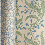 Folded printed linen in a wavy floral stripe design in light blue on white, along side another larger scale floral fabric. 