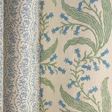 Folded printed linen in a wavy floral stripe design in light blue on white, along side another larger scale floral fabric. 