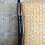 Wooden chair with a yellow floral fabric against wallpaper in a pastel floral pattern.