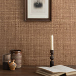 Detail of a styled tabletop scene with ceramic cups, open book and candlestick against a brown textural wallpaper with framed antique black and white portrait of a man in black and white. 