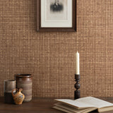 Detail of a styled tabletop scene with ceramic cups, open book and candlestick against a brown textural wallpaper with framed antique black and white portrait of a man in black and white. 