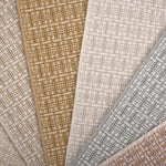 A close-up fan arrangement of basketweave pattern carpet samples in beige, tan, cream, light blue-gray, and dusty rose tones.