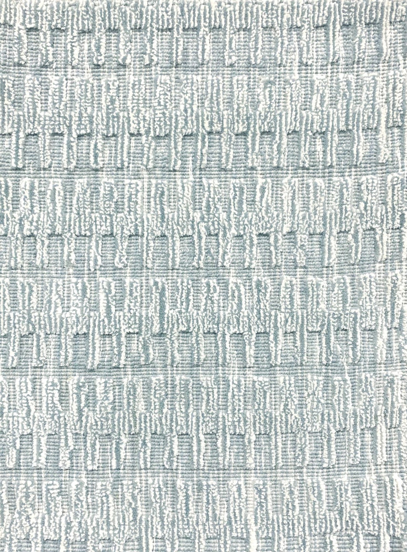 A close-up of a broadloom rug in a vertical ribbed pattern  in a neutral mix of off-white, and aqua blue.