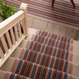 Overhead image of a stair case and landing with a runner and area rug in a complex woven striped made of wool in shades of blue and red. 