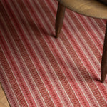Detail of an area rug in a complex woven striped runner made of wool in shades of red.