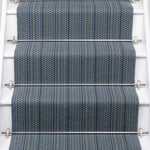 A close-up view of a staircase with carpeted steps in a blue-gray stripe pattern, bordered by white risers,