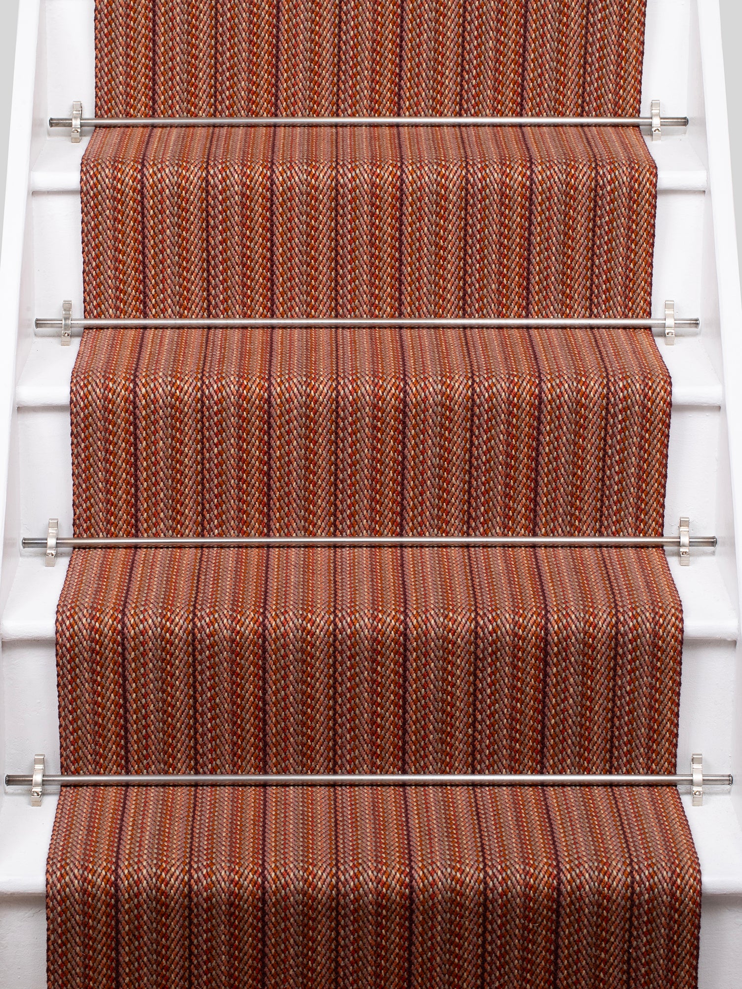 A close-up view of a staircase with carpeted steps in a red-orange stripe pattern, bordered by white risers.