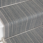 Close-up of carpeted stairs with a textured herringbone pattern in gray and blue tones, showing the stair treads and metal rail.