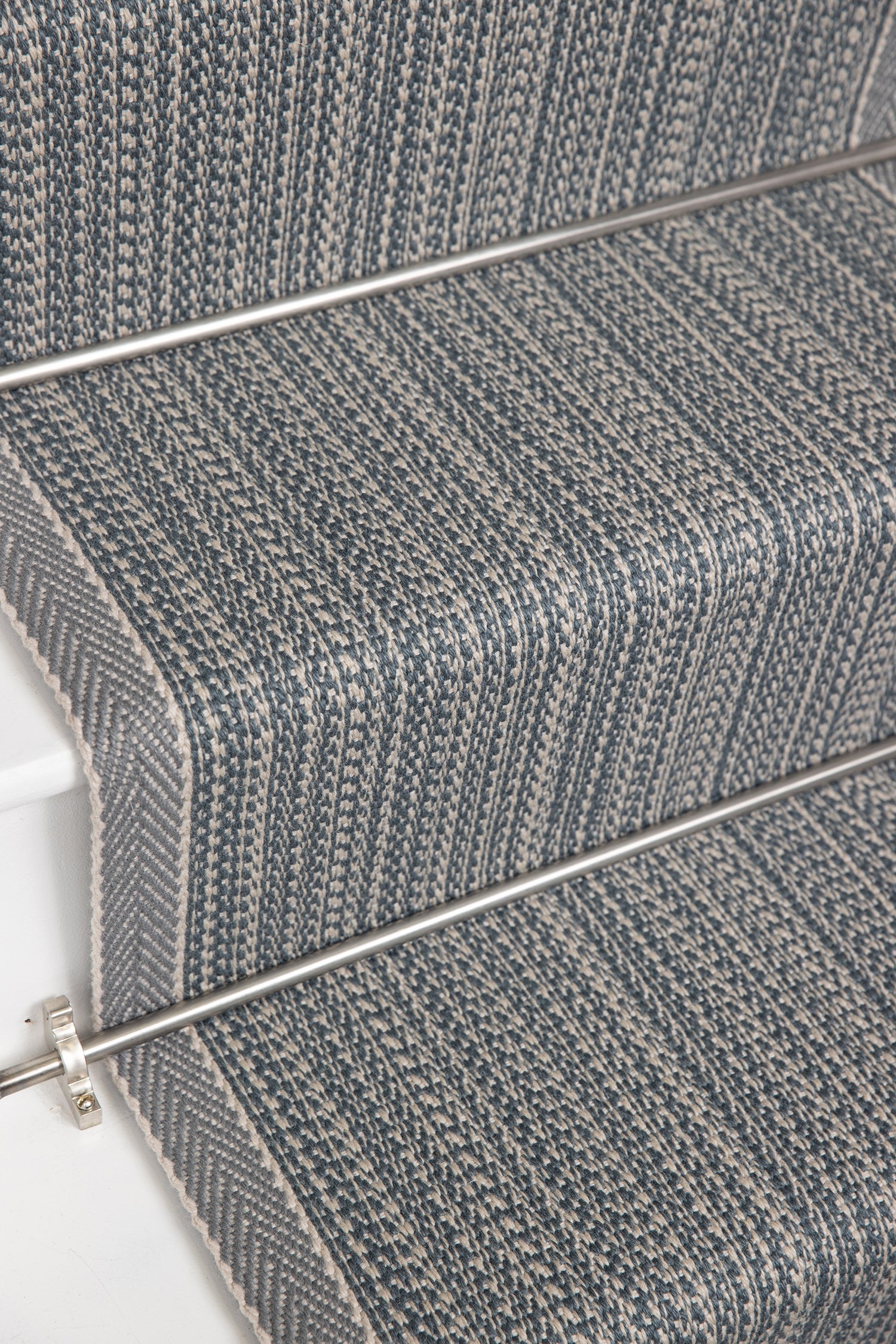 Close-up of carpeted stairs with a textured herringbone pattern in gray and blue tones, showing the stair treads and metal rail.