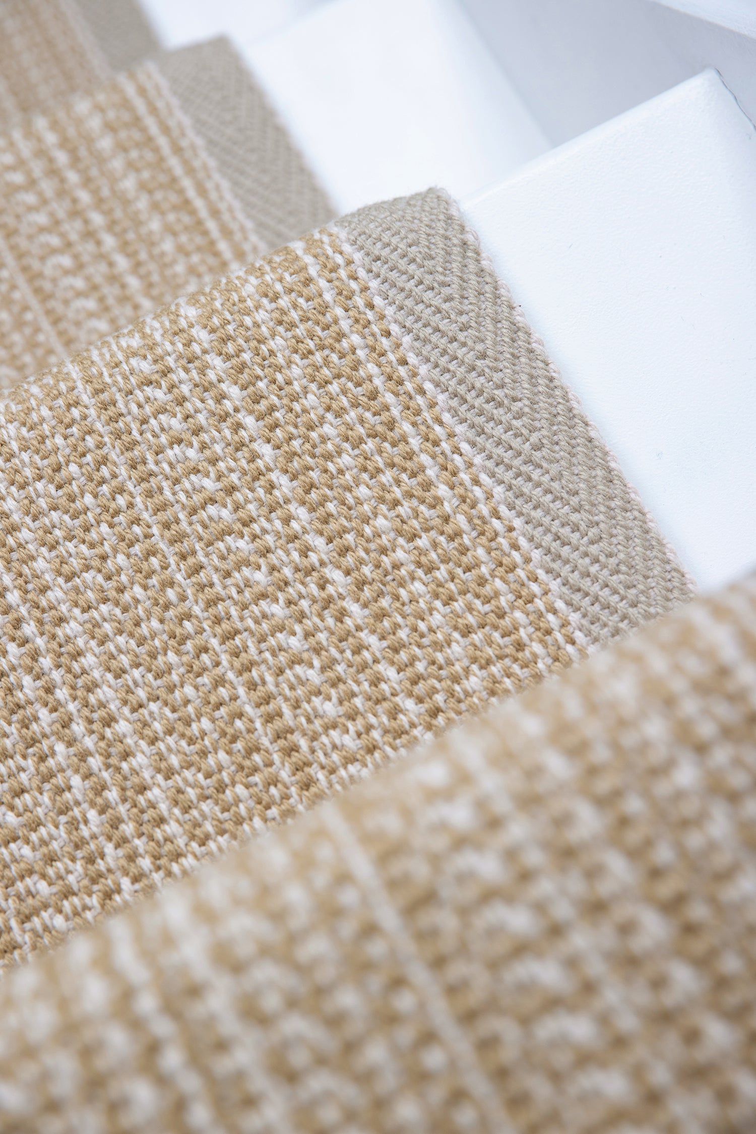 Close-up of flatweave stair runner in warm beige and cream tones, with the stair white surface visible behind them.