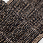 A close-up of a flatweave stair runner with a subtle herringbone pattern and a lighter tan border, laid diagonally on white stairs.