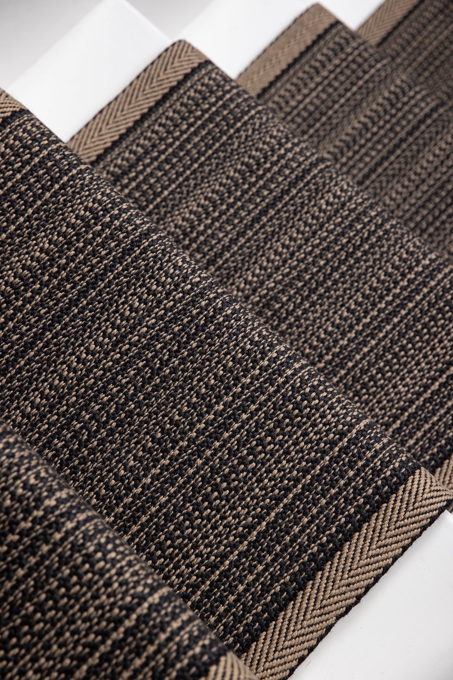 A close-up of a flatweave stair runner with a subtle herringbone pattern and a lighter tan border, laid diagonally on white stairs.