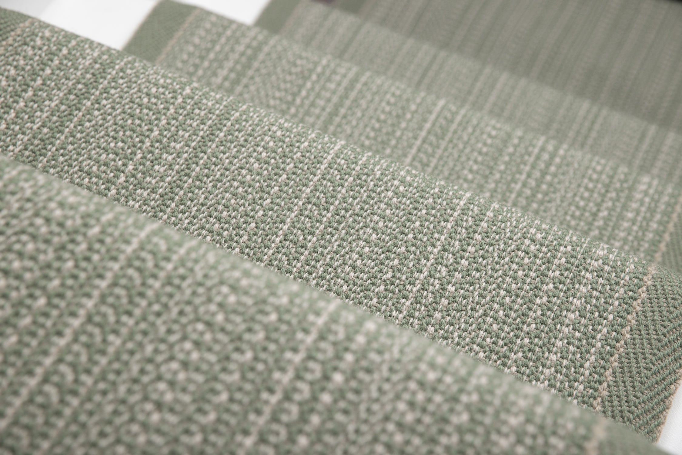 A close-up of a stair runner sample in a muted sage green color textural stripe.