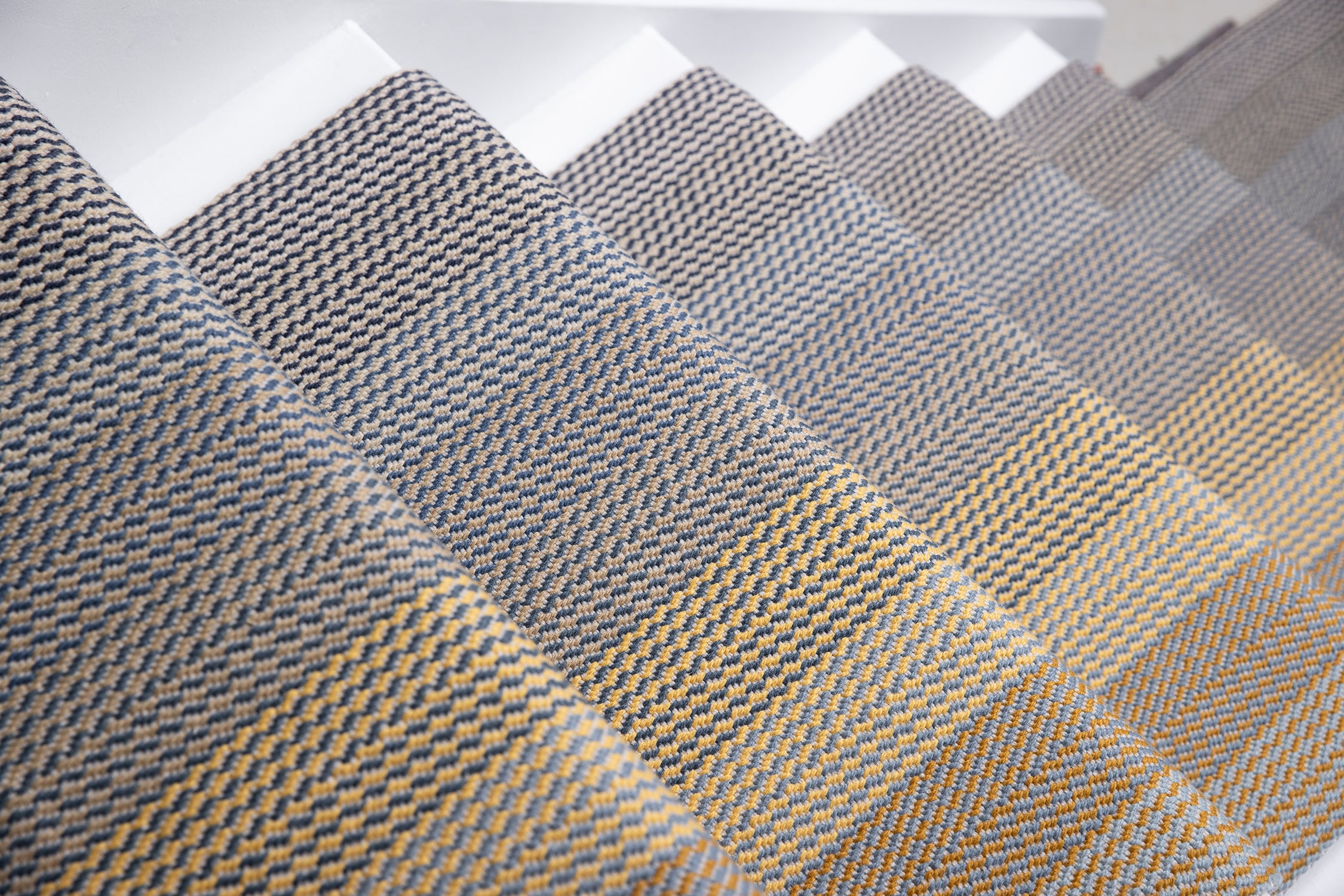 Close-up of carpeted stair treads with a woven herringbone pattern in gray, beige, and brown tones.