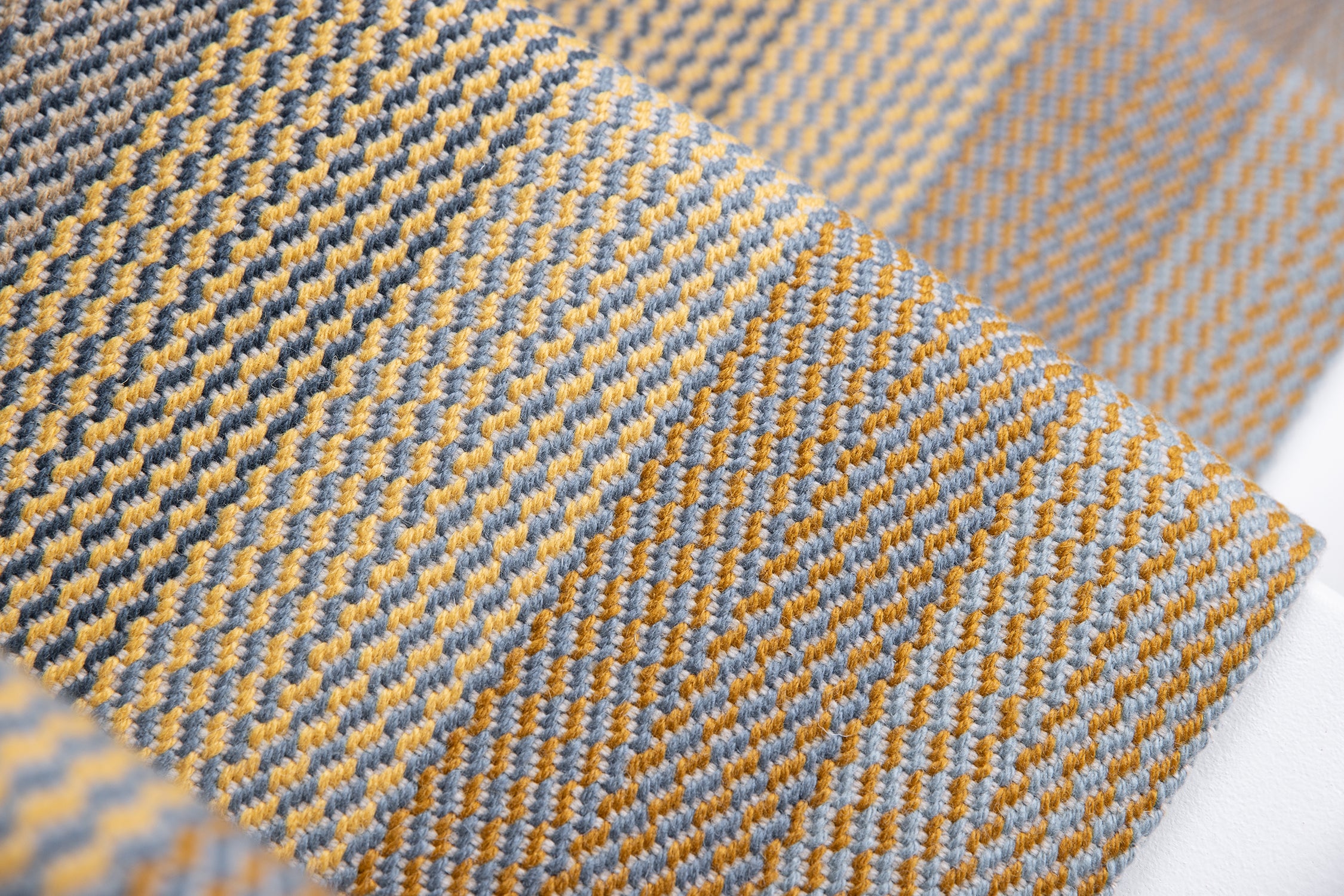 A close-up of a woven stair runner with a herringbone pattern in mustard yellow, light gray, and dark charcoal.