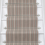 White stair case with a runner in a complex woven stripe design of wool in shades of pink and grey.