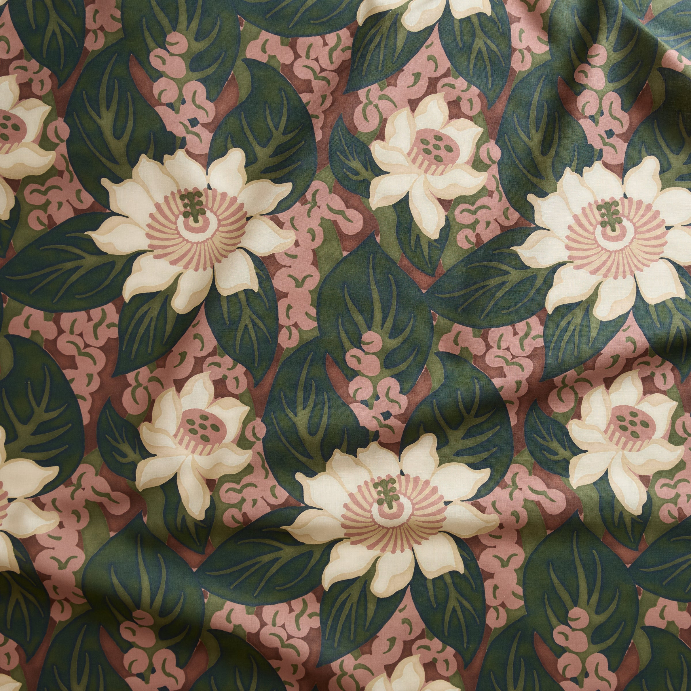 Close up of tropical floral gently draped printed linen featuring cream-colored blossoms with pink centers, dark green leaves on a brick red background.