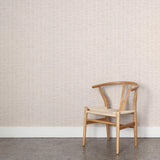A wooden chair stands in front of a wall papered in a small-scale checked pattern in shades of cream.