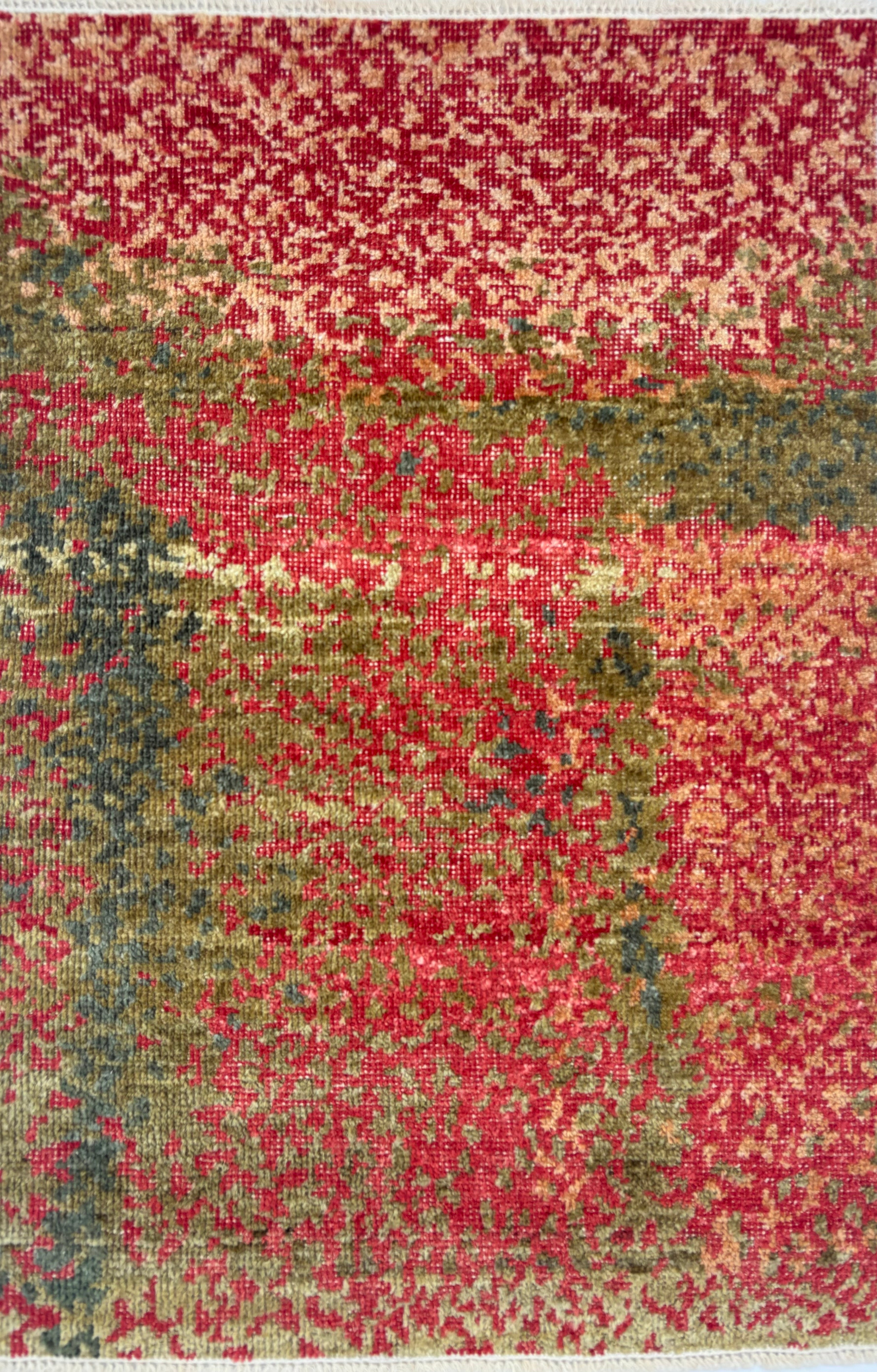 Handknotted rug sample in a pointillist textural design in shades of green, teal and tan on a red field. 