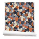 Partially unrolled wallpaper in a painterly geometric pattern in shades of blue, cream and rust.