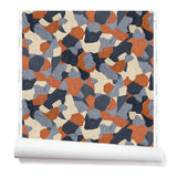 Partially unrolled wallpaper in a painterly geometric pattern in shades of blue, cream and rust.